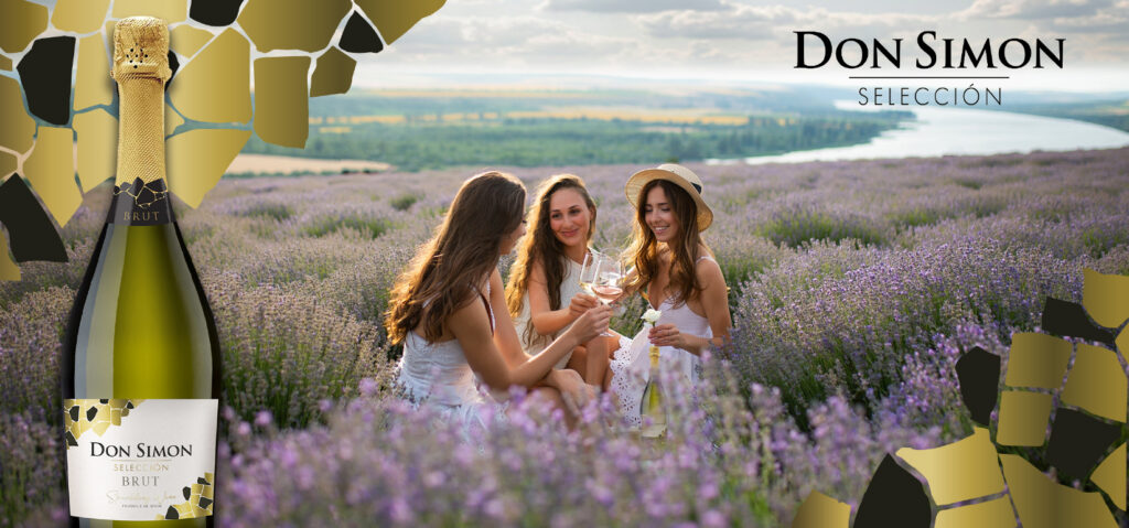 Three women in white dresses sit in a lavender field, smiling and enjoying glasses of sparkling wine. A Don Simon Brut bottle is featured in the foreground with a scenic river and hills in the background.